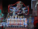 Lo Manthang Thubchen 05-3 Main Assembly Hall Hayagriva Statue To the right of Amitayus is a statue of red Hayagriva in yam-yum with his consort in the main assembly hall at Thubchen Gompa in Lo Manthang. Hayagriva, a fierce form of the compassionate Avalokiteshvara, has huge wings, three heads crowned with skulls, six arms and four legs, and a horse head in his hair, which gives him his name horse-necked one. Hayagriva wears a belt strung with freshly severed heads, a lion skin loincloth. In his front left hand he holds a skull cup filled with transformed blood and guts of sentient beings and in his front right hand a vajra.
